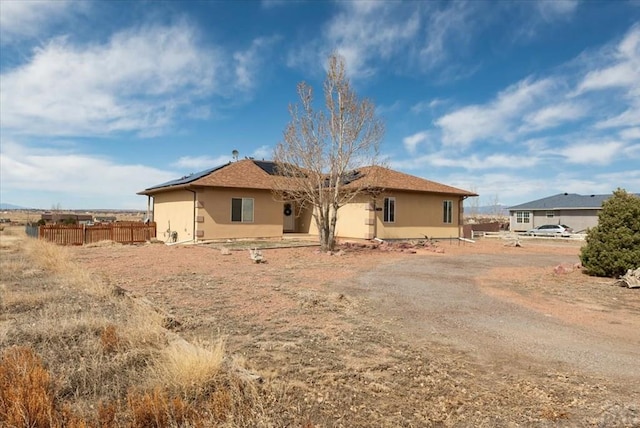 rear view of property with stucco siding, roof mounted solar panels, and fence