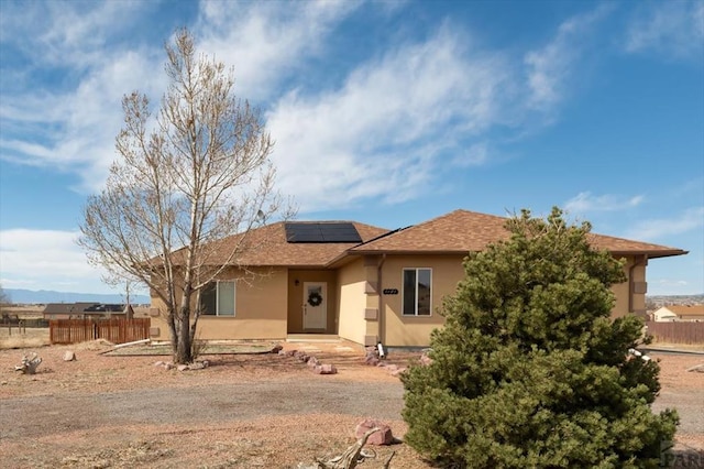 view of front of house with fence, roof mounted solar panels, and stucco siding