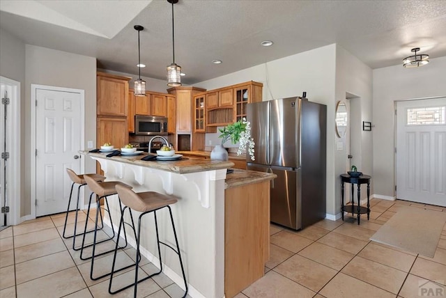 kitchen featuring a kitchen island with sink, appliances with stainless steel finishes, a breakfast bar area, light tile patterned floors, and glass insert cabinets