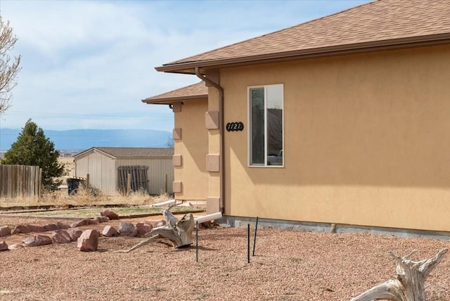 view of side of property with stucco siding, roof with shingles, and fence