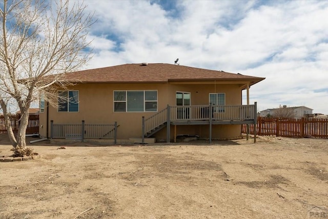 back of property featuring stucco siding, a shingled roof, a deck, and fence