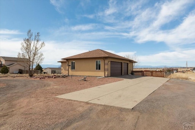 view of side of property with stucco siding, an attached garage, driveway, and fence