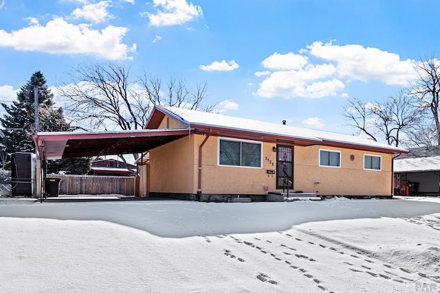 view of front of home with an attached carport, fence, and stucco siding