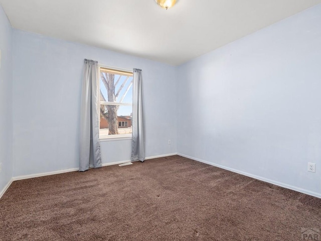 spare room with dark colored carpet, visible vents, and baseboards