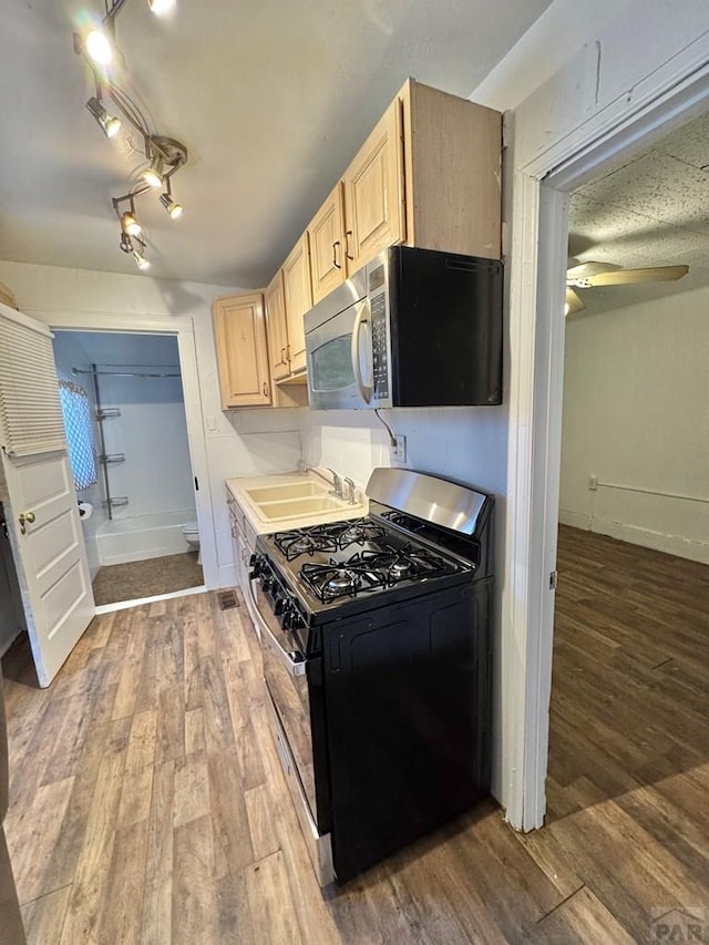 kitchen with range with gas stovetop, stainless steel microwave, light brown cabinetry, dark wood-type flooring, and a sink