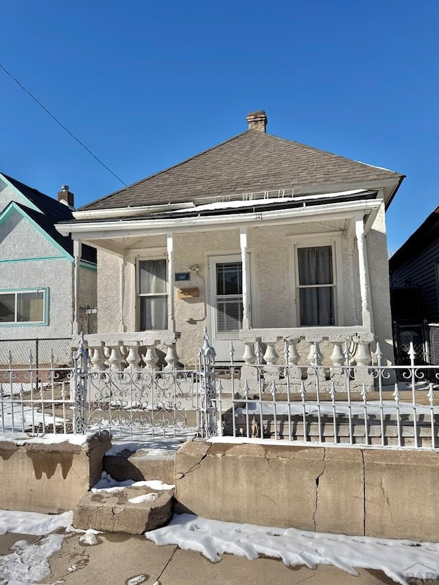 bungalow-style home featuring covered porch, a fenced front yard, stucco siding, and roof with shingles