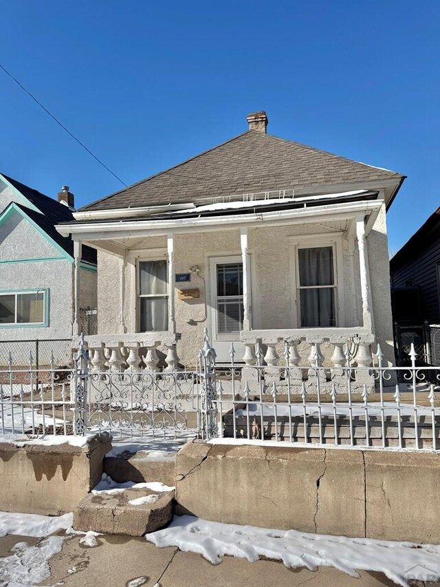 bungalow-style home featuring covered porch, a fenced front yard, stucco siding, and roof with shingles