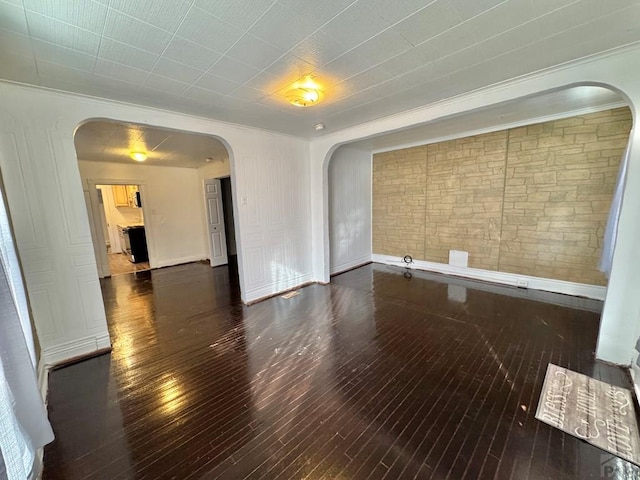 unfurnished room featuring dark wood-style floors, arched walkways, and baseboards