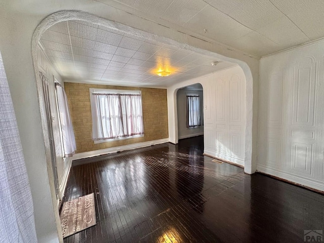 spare room with brick wall, baseboards, arched walkways, and dark wood-type flooring