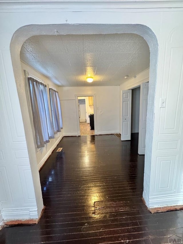 unfurnished room with arched walkways, dark wood-style flooring, and baseboards