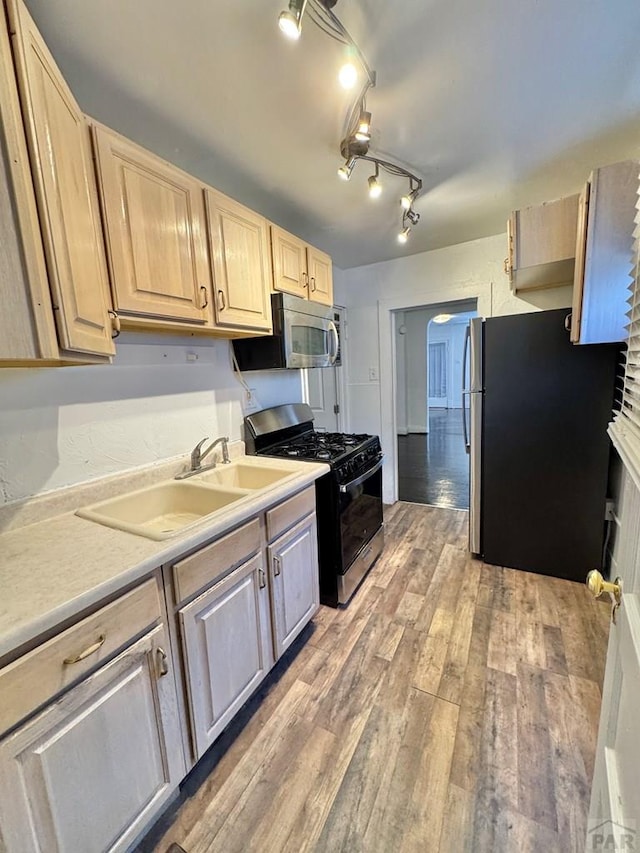 kitchen featuring appliances with stainless steel finishes, light countertops, a sink, and light brown cabinetry