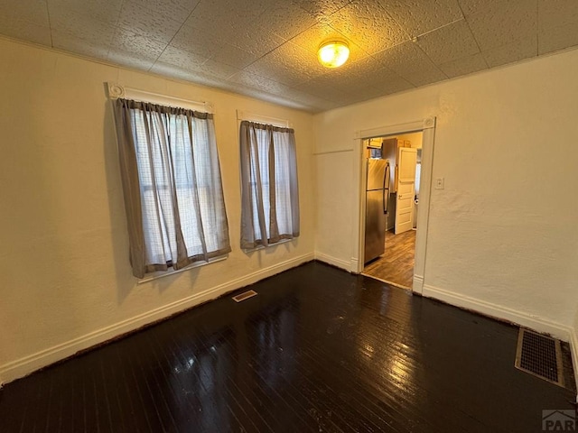 empty room featuring baseboards, visible vents, and wood finished floors