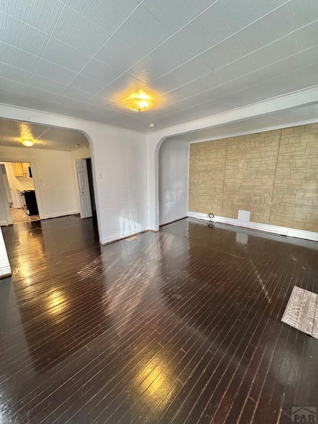 spare room with dark wood-type flooring, arched walkways, and brick wall