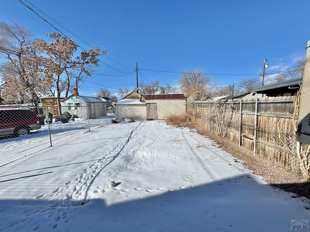 snowy yard featuring a storage unit, an outdoor structure, and fence