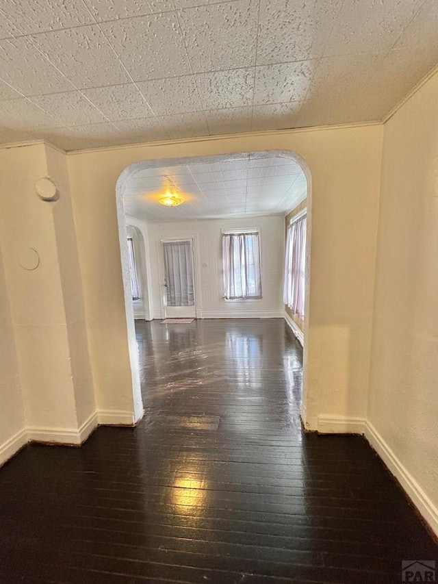 unfurnished room with dark wood-type flooring, arched walkways, and baseboards