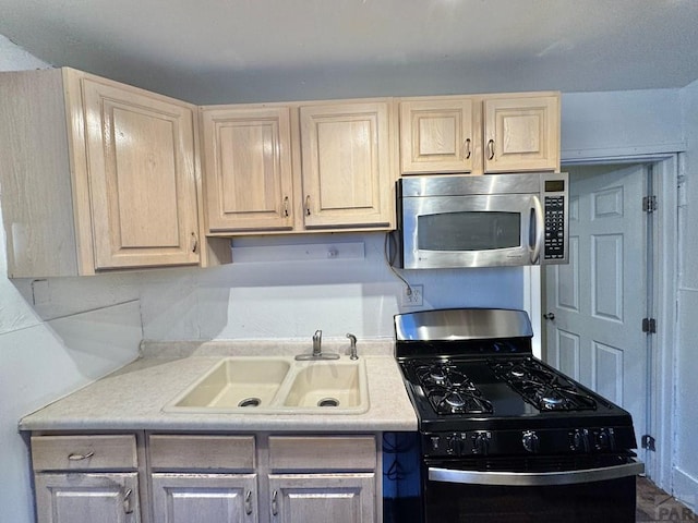 kitchen with a sink, light countertops, black range with gas stovetop, light brown cabinetry, and stainless steel microwave