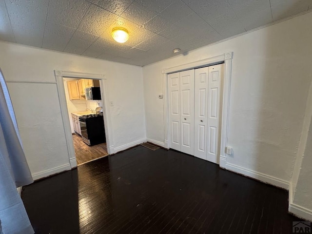 unfurnished bedroom featuring a closet, dark wood finished floors, and baseboards