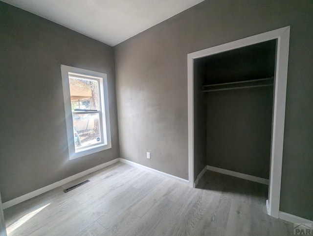 unfurnished bedroom featuring light wood-type flooring, baseboards, visible vents, and a closet