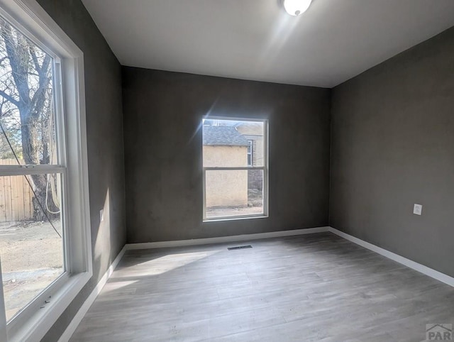 unfurnished room with wood finished floors, visible vents, and baseboards