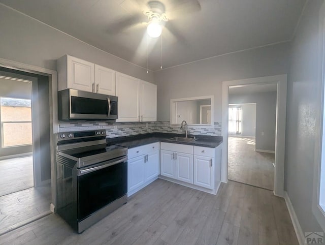 kitchen featuring decorative backsplash, white cabinets, dark countertops, appliances with stainless steel finishes, and a sink