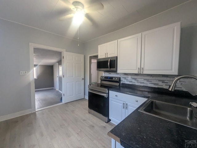 kitchen featuring dark countertops, decorative backsplash, appliances with stainless steel finishes, white cabinets, and a sink