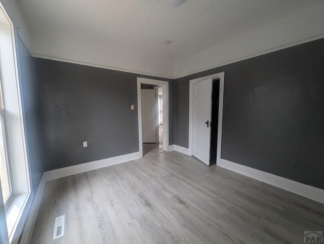 empty room with visible vents, light wood-style flooring, and baseboards