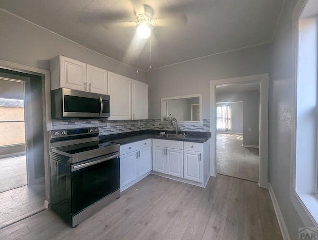 kitchen featuring tasteful backsplash, dark countertops, appliances with stainless steel finishes, white cabinetry, and a sink