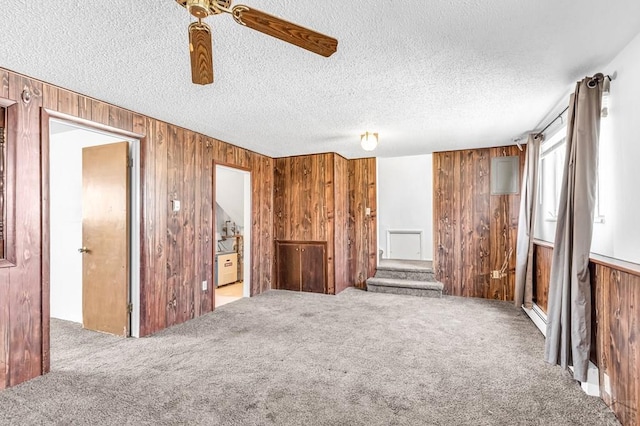 unfurnished living room with a textured ceiling, carpet flooring, and wood walls