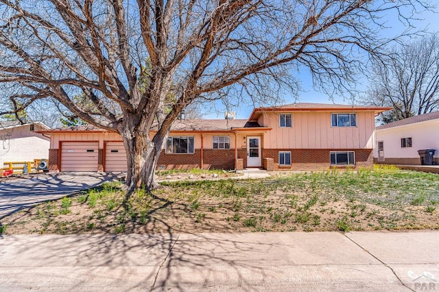 tri-level home with board and batten siding, driveway, brick siding, and a garage