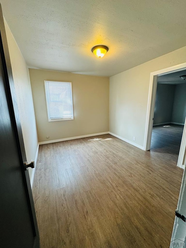 spare room featuring wood finished floors, baseboards, and a textured ceiling