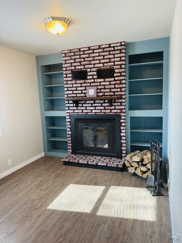 unfurnished living room with a brick fireplace, baseboards, built in features, and wood finished floors