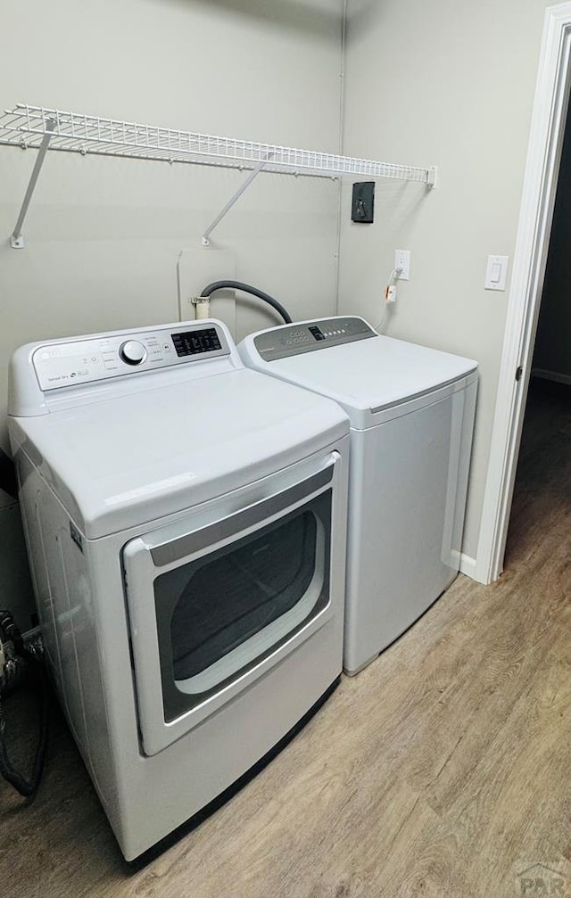 clothes washing area featuring washer and dryer, laundry area, baseboards, and light wood finished floors