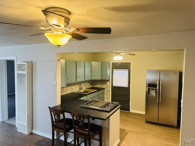 kitchen featuring dark countertops, light wood-style flooring, appliances with stainless steel finishes, a sink, and green cabinetry