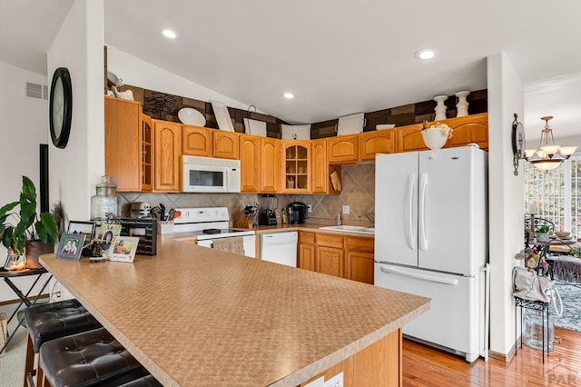 kitchen with white appliances, glass insert cabinets, a peninsula, visible vents, and a sink