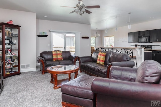 living room featuring ceiling fan with notable chandelier, visible vents, baseboards, and light colored carpet