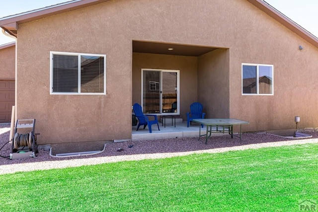 rear view of property featuring a lawn, a patio, and stucco siding