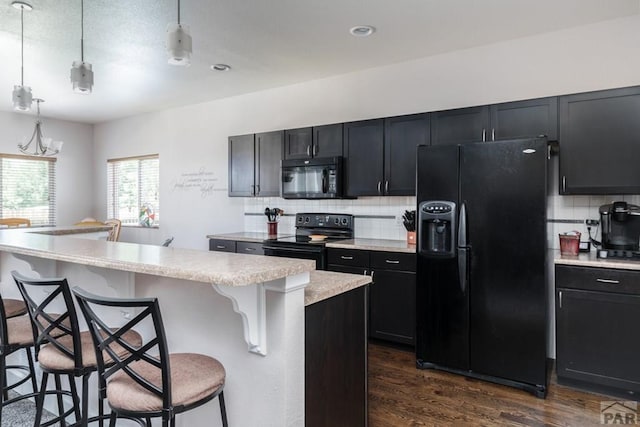 kitchen with a breakfast bar area, light countertops, a center island, dark wood-style floors, and black appliances