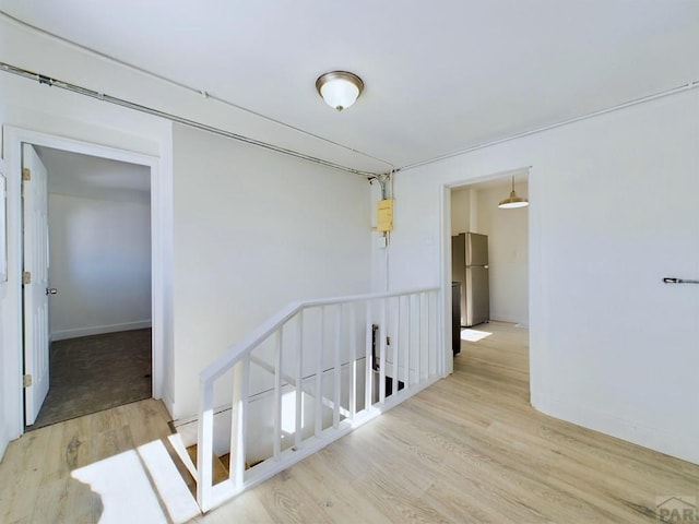 corridor featuring an upstairs landing, baseboards, and light wood finished floors