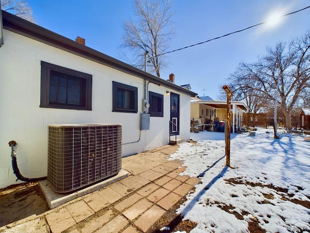 snow covered back of property featuring a chimney, stucco siding, and central air condition unit