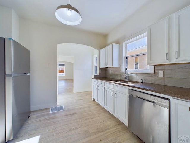 kitchen featuring arched walkways, stainless steel appliances, visible vents, white cabinets, and a sink