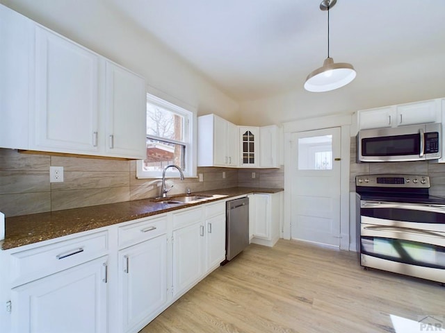 kitchen with appliances with stainless steel finishes, white cabinetry, glass insert cabinets, and a sink