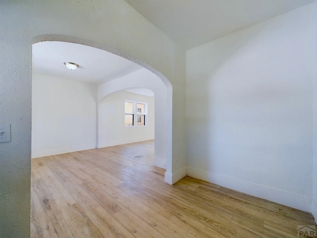 spare room with light wood-style floors, arched walkways, and visible vents