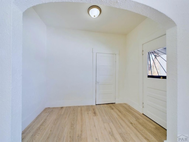 empty room featuring light wood-type flooring, baseboards, and arched walkways