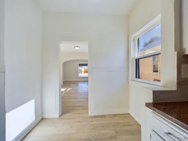 corridor featuring arched walkways, baseboards, and light wood-style floors