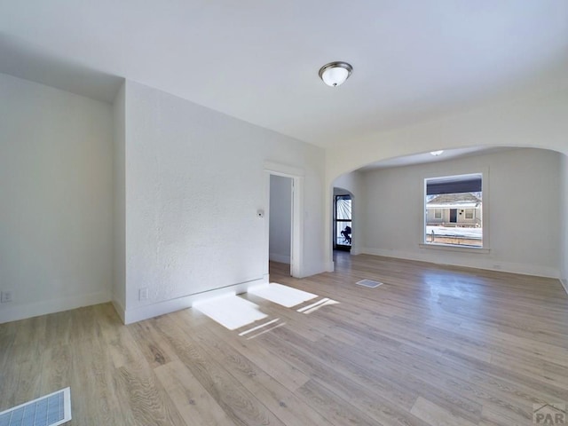 empty room featuring arched walkways, light wood finished floors, visible vents, and baseboards