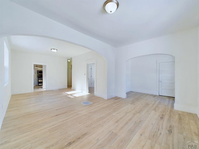 spare room featuring arched walkways, light wood-style flooring, and visible vents