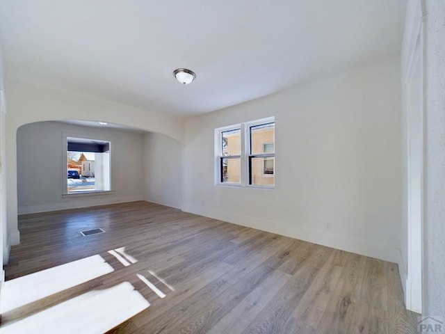 empty room featuring arched walkways, light wood-type flooring, visible vents, and baseboards