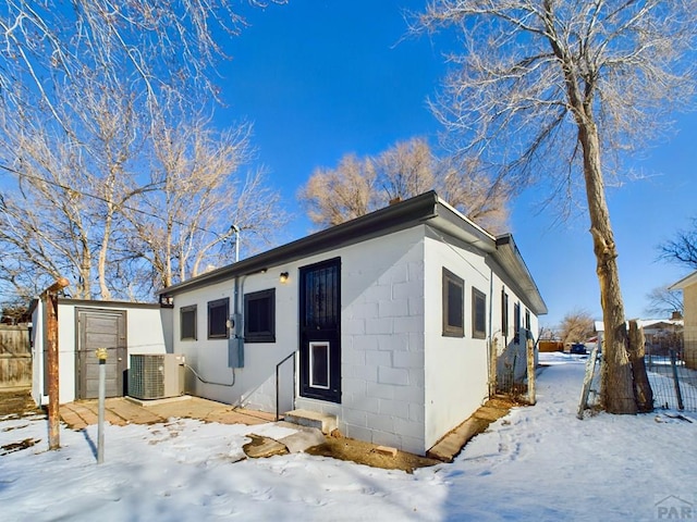 snow covered back of property with entry steps, concrete block siding, cooling unit, and fence