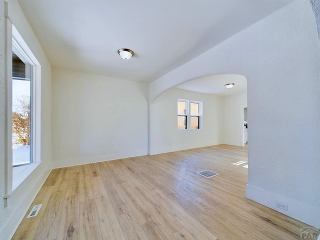 unfurnished room featuring light wood-style floors, visible vents, and arched walkways