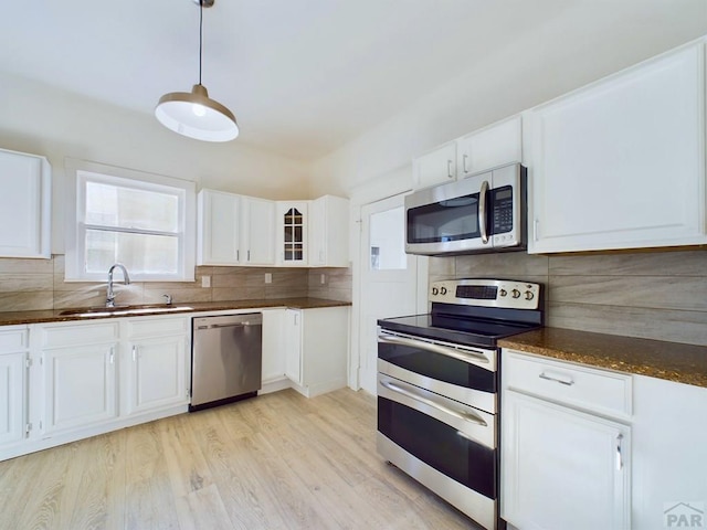 kitchen with appliances with stainless steel finishes, a sink, glass insert cabinets, and white cabinets